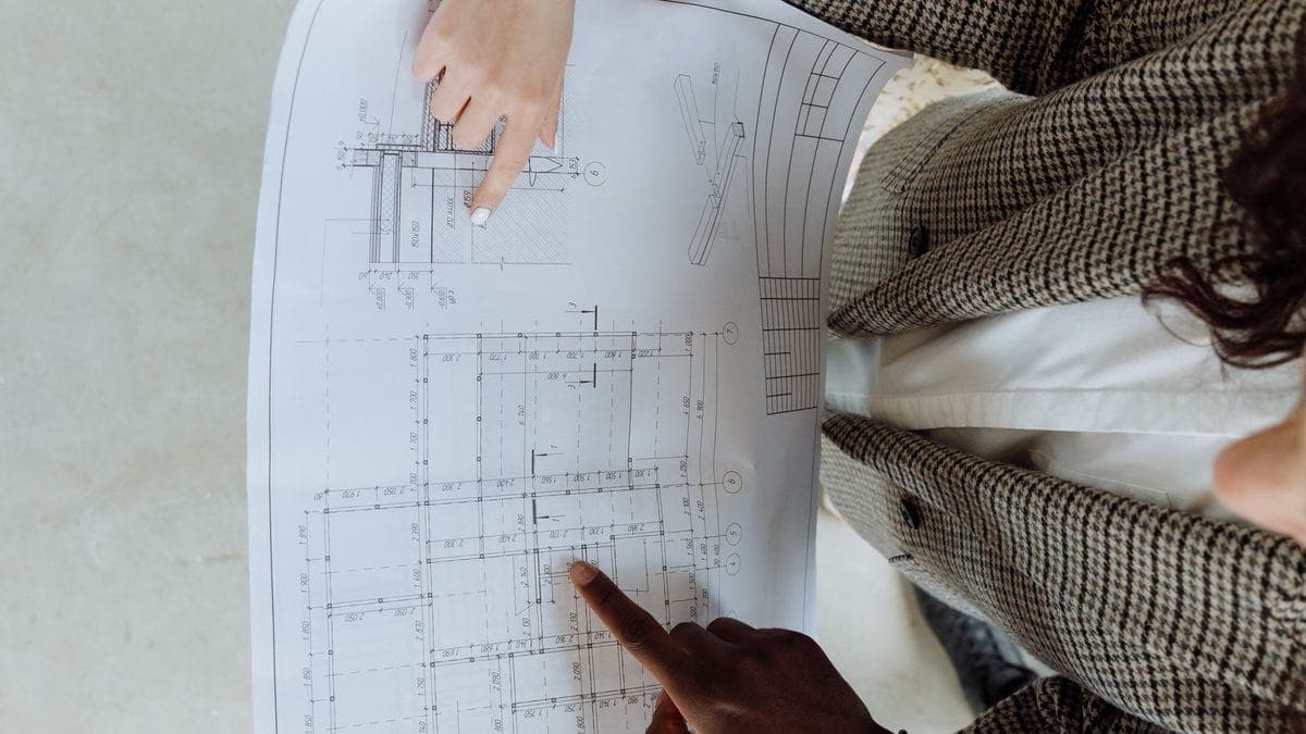 Two people pointing at and reviewing an architectural blueprint together, seen from above