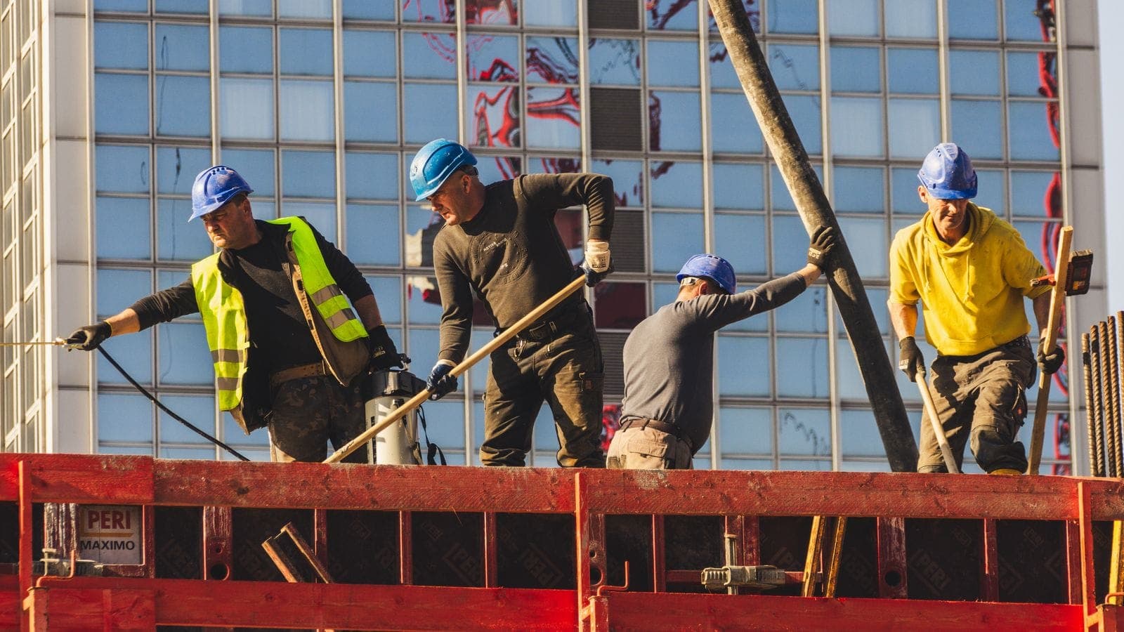 Construction workers in hard hats and safety vests actively working on a high-rise building site