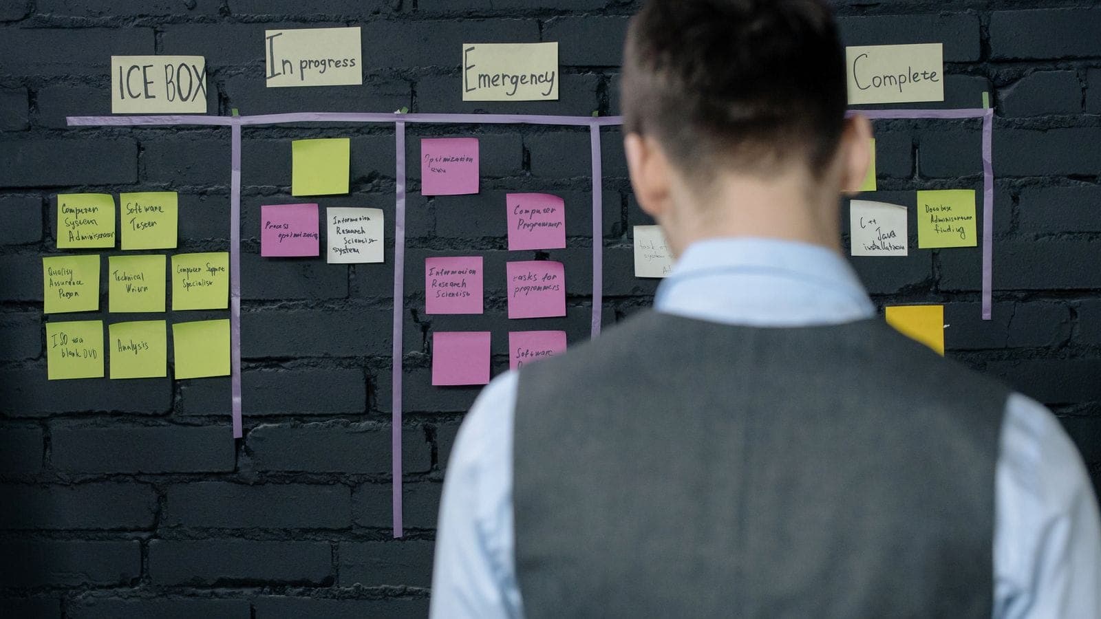 Professional standing in front of a wall-mounted project planning board covered in sticky notes