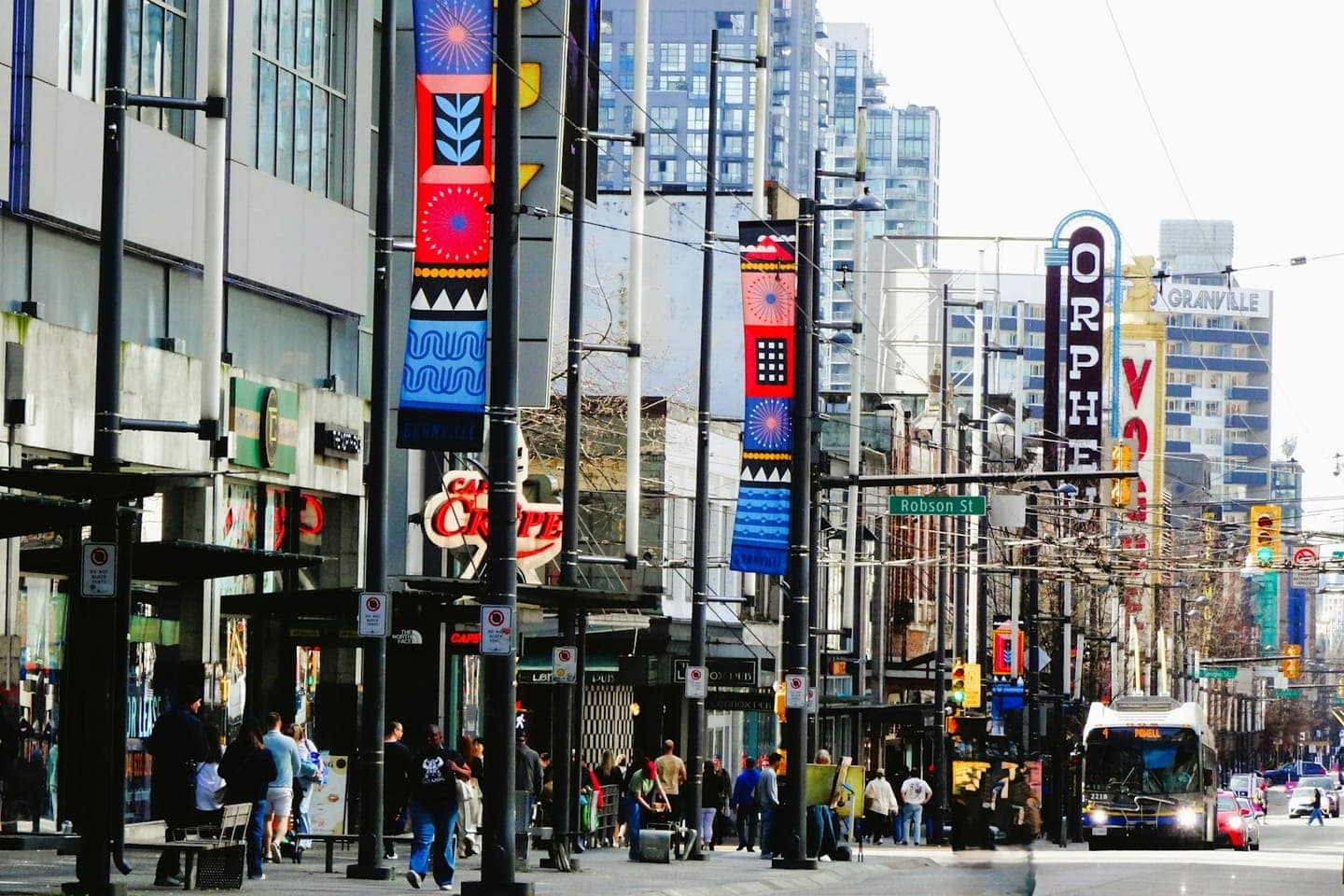 Busy urban shopping street lined with multiple storefronts and bright signage