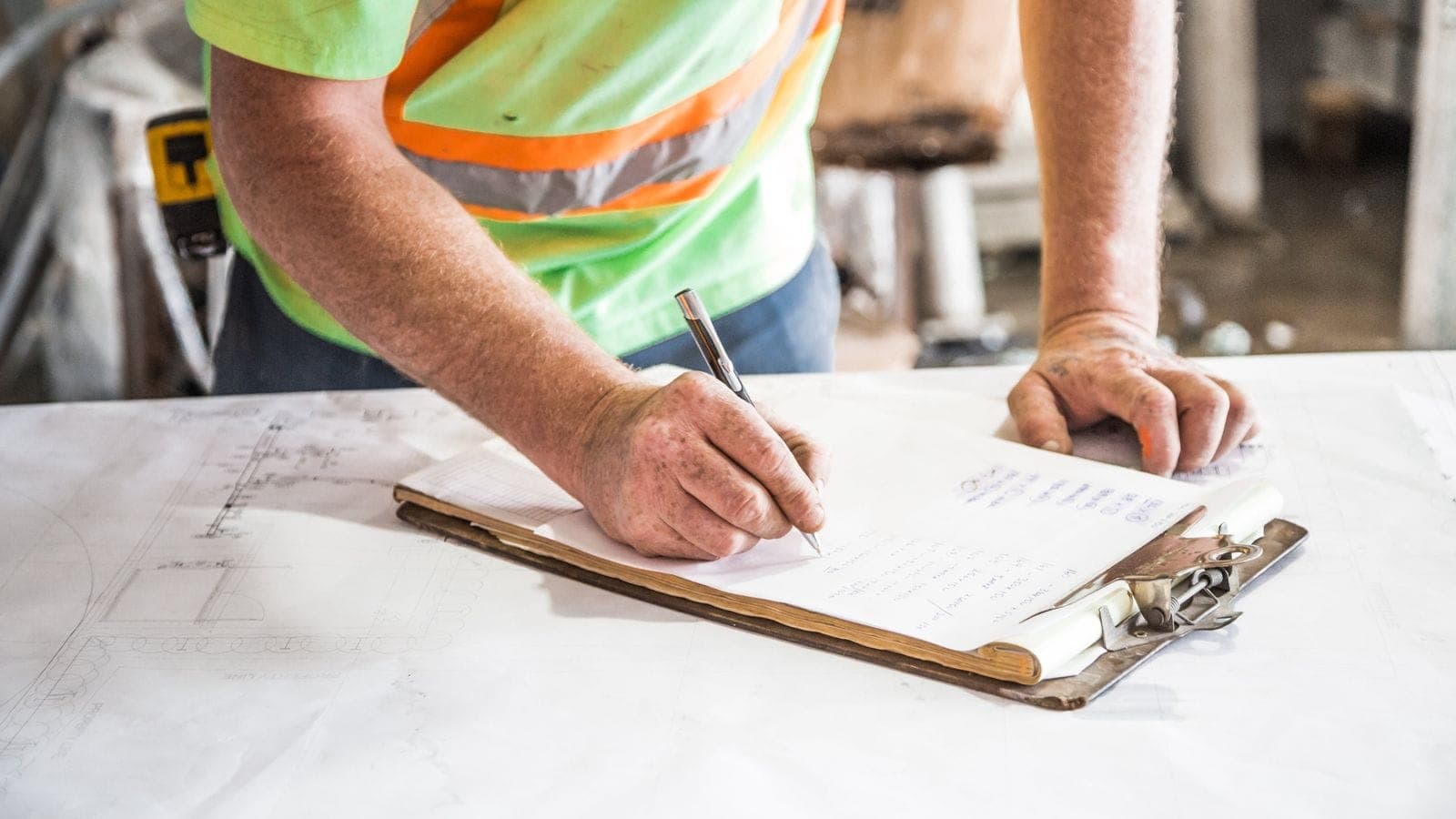 Construction worker writing inspection notes on a clipboard at a job site