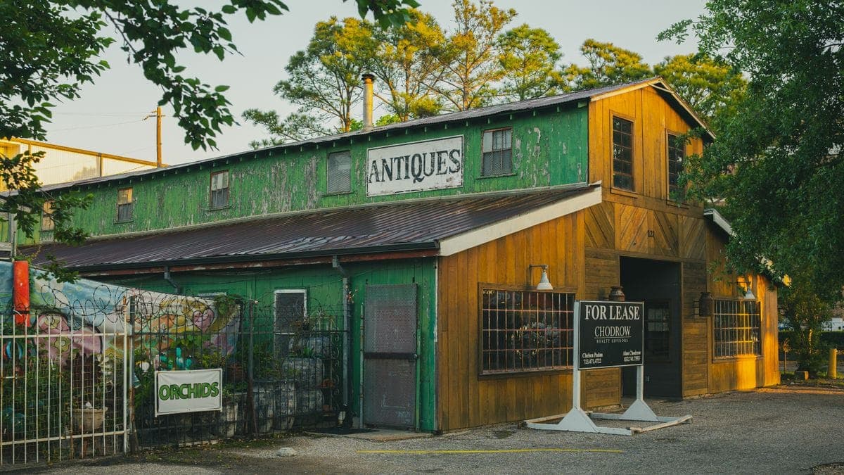 A shuttered green-and-wood antiques store with a For Lease real-estate sign out front