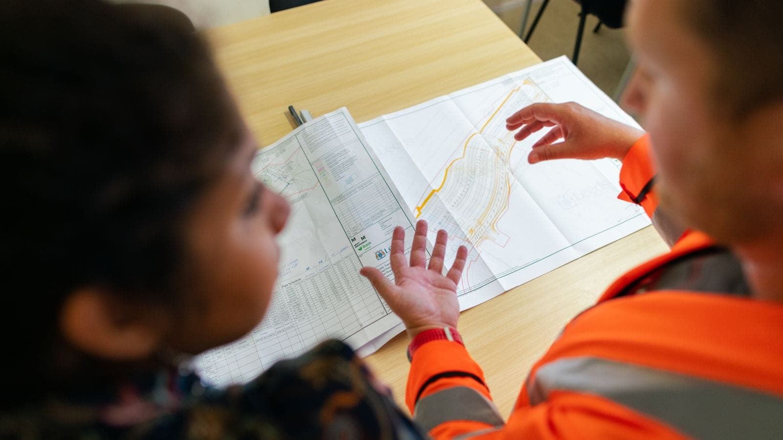 Two workers in high-visibility gear reviewing and pointing at a construction site plan on a table