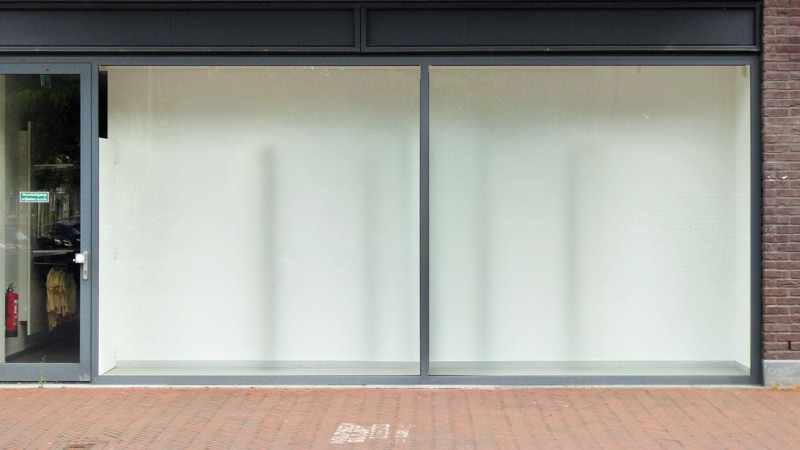 Empty modern retail storefront with large glass windows on a city street, available for lease