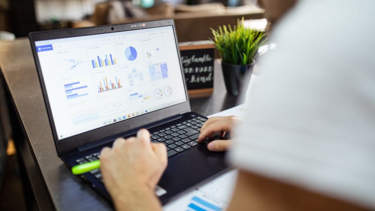 A person working on a laptop that displays a dashboard of charts and graphs on an office desk