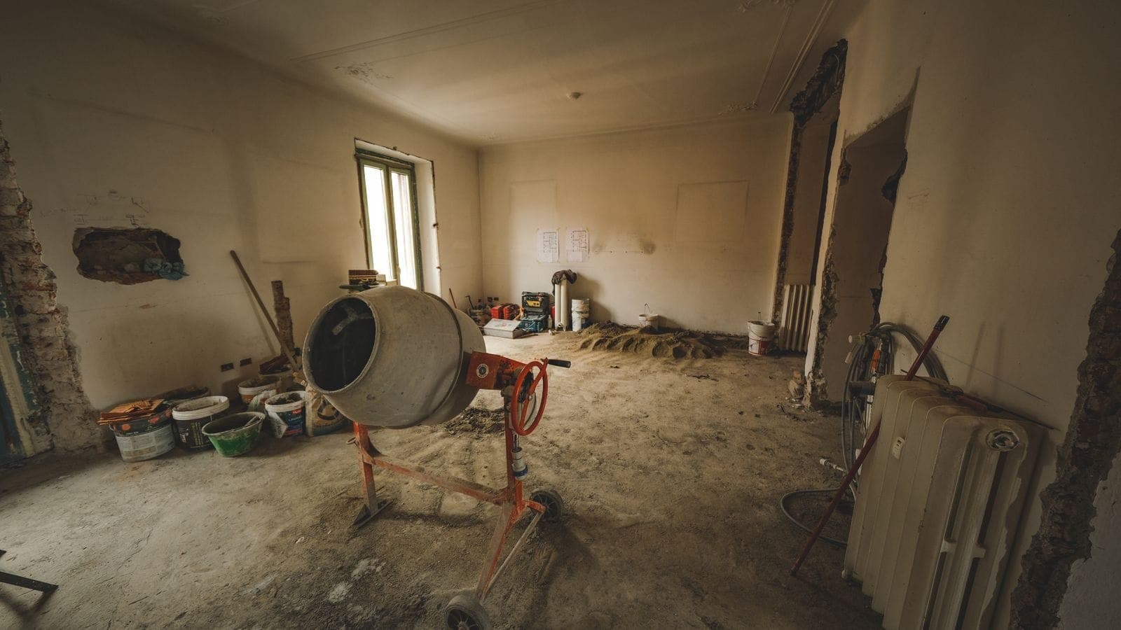 Unfinished commercial interior mid-buildout with bare walls, a concrete mixer, and construction tools