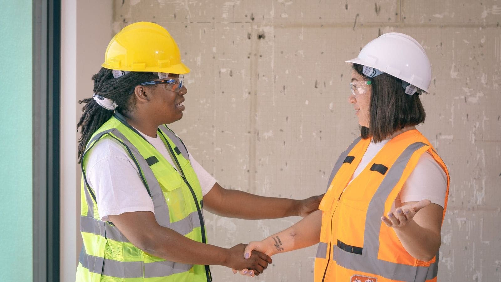 Two workers in hard hats and hi-vis vests shaking hands on a construction site