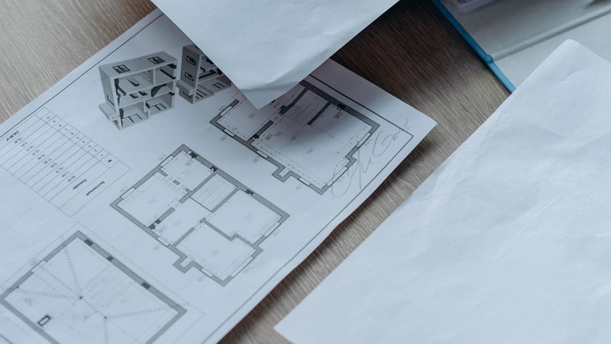 Architectural floor plans and a small building model spread across a wooden desk