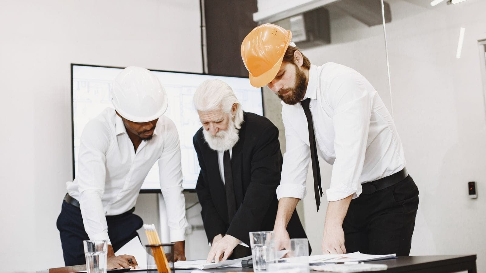 Team of architects in hard hats reviewing construction blueprints together around a table in a modern office
