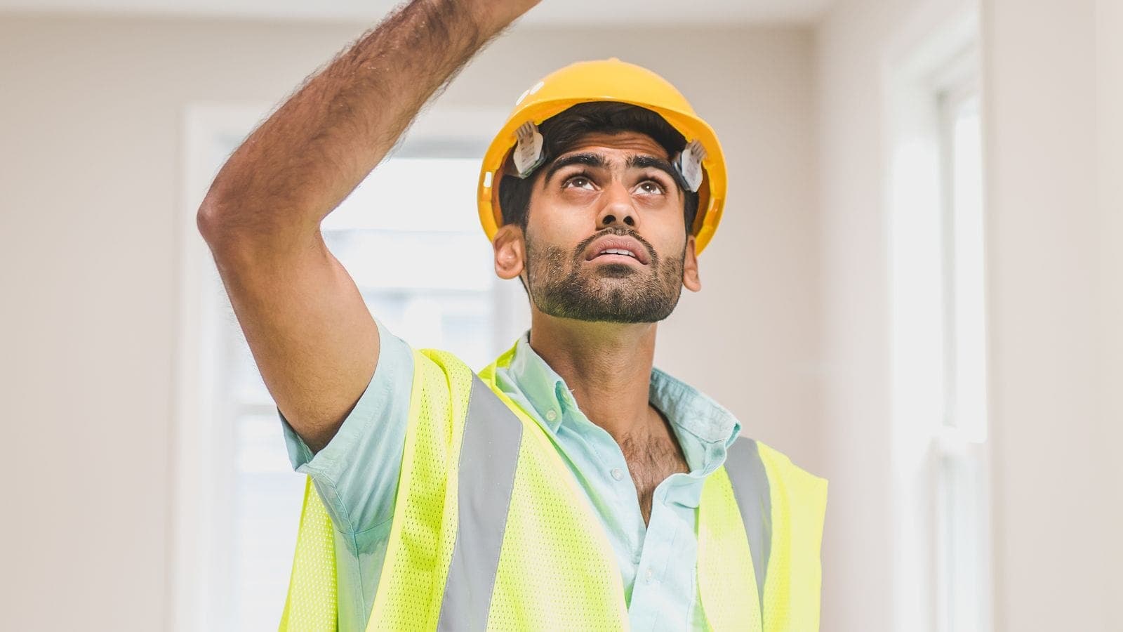 Construction worker in a yellow hardhat and safety vest inspecting an interior ceiling during a final walkthrough